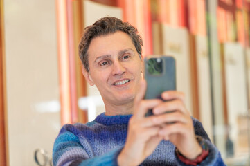 Smiling man using smartphone taking selfie wearing blue sweater