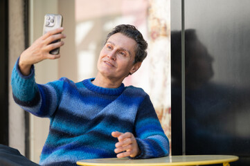 Mature man taking a selfie with smartphone sitting at the table of an outdoor cafe