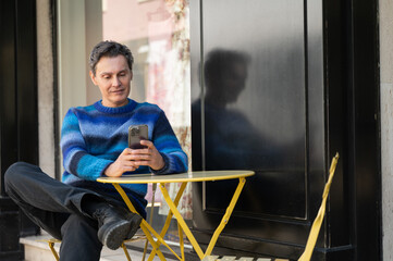 Man using smartphone sitting at yellow table outside a shop
