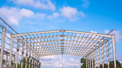 Metal column and roof beam structure of warehouse industrial factory building in construction site against blue sky background, Front view with copy space