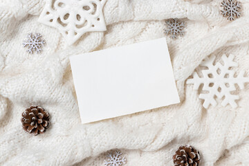 Horizontal blank card on white knitted sweater near Christmas decor, winter Holiday mockup