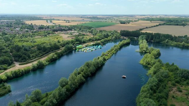Aerial close up drone shot beautiful blue lakes and lush greenery with inflatable aqua water park play event near Little Paxton England UK