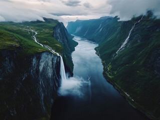 A dramatic aerial scene of a deep Norwegian fjord framed by towering cliffs and lush greenery, with a powerful waterfall cascading into a serene, dark blue river below.

