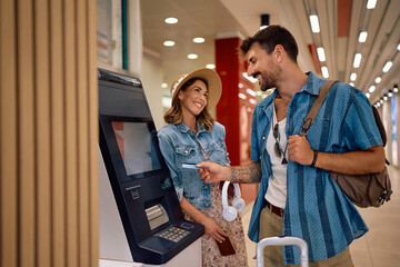 Happy couple withdrawing cash at airport terminal.