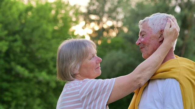 A loving senior woman gently touches her husband's face in a tender moment outdoors, surrounded by nature.