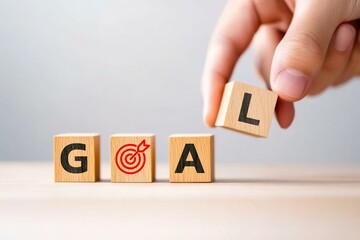 A hand placing the letter L on wooden blocks spelling the word GOAL, symbolizing ambition and achievement in personal or professional development.