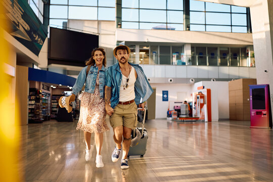 Couple of travelers holding hands while rushing to catch their flight at airport.