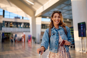 Happy traveler waiting for her flight at airport and looking at camera.