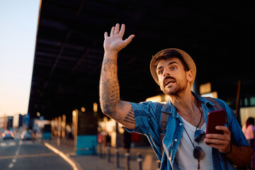 Mid adult man with arm raised trying to catch a cab at the station.