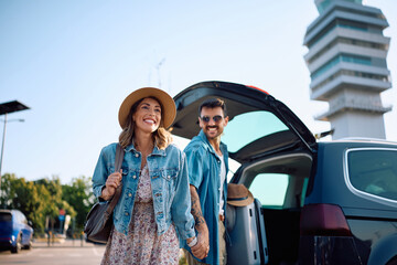 Happy couple taking their luggage from a car at airport parking lot.