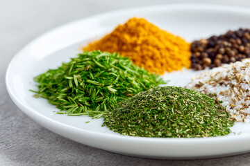 Assorted spices and herbs presented on white plate, food ingredients for culinary creations 