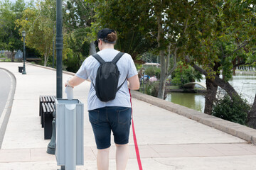 Woman with cap and backpack throws empty beer cans in trash during walk with dog, helping clean up the park.