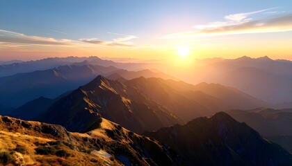 Golden sunrise over a vast, hazy mountain range, creating layers of warm light and shadow across the landscape.