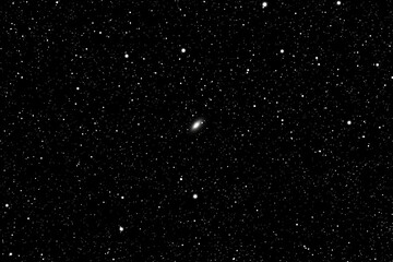 A distant galaxy, a faint smudge, amidst a dense field of stars