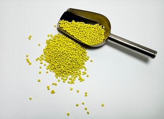 Yellow plastic masterbatch, polymer carries colorful pigments with small scoops poured into a white background, suitable for product catalog design of industrial plastic manufacturing company profiles