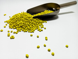 Yellow plastic masterbatch, polymer carries colorful pigments with small scoops poured into a white background, suitable for product catalog design of industrial plastic manufacturing company profiles