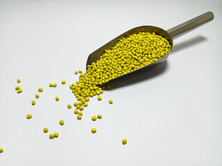 Yellow plastic masterbatch, polymer carries colorful pigments with small scoops poured into a white background, suitable for product catalog design of industrial plastic manufacturing company profiles