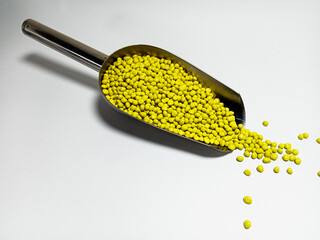 Yellow plastic masterbatch, polymer carries colorful pigments with small scoops poured into a white background, suitable for product catalog design of industrial plastic manufacturing company profiles