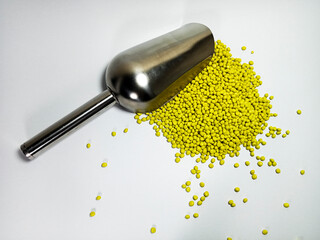 Yellow plastic masterbatch, polymer carries colorful pigments with small scoops poured into a white background, suitable for product catalog design of industrial plastic manufacturing company profiles