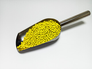 Yellow plastic masterbatch, polymer carries colorful pigments with small scoops poured into a white...