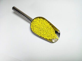 Yellow plastic masterbatch, polymer carries colorful pigments with small scoops poured into a white background, suitable for product catalog design of industrial plastic manufacturing company profiles