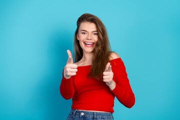Cheerful young girl with brown hair wearing a red top, posing playfully against a vibrant blue...