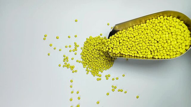 Pouring yellow masterbatch granules into a white background medium with a stainless scoop, suitable for videography design of plastic industry company profiles