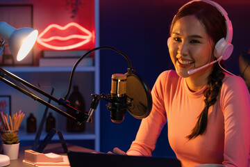 Smiling creative young beautiful Asian influencer talking in channel with positive podcast speech...