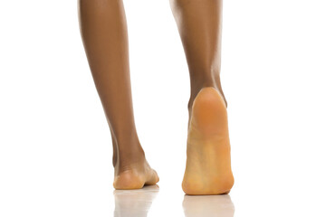 Close-up rear view of black woman's bare feet walking with visible sole, clean and healthy skin,...