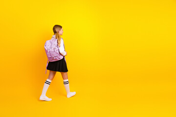 Smiling schoolgirl carrying her backpack on a vibrant yellow background creating a cheerful back-to-school atmosphere
