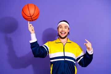Young male athlete spins a basketball while wearing vintage tracksuit on a vibrant purple...