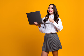 Smiling businesswoman with laptop promoting content against a yellow background and pointing...