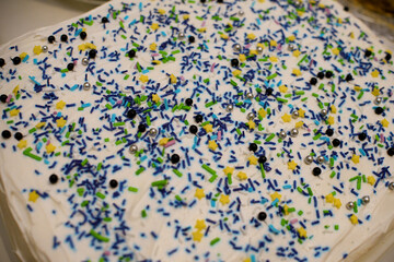 Square-shaped cake decorated with white whipped cream, colorful crumbs, beads, and yellow stars