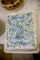 Square-shaped cake decorated with white whipped cream, colorful crumbs, beads, and yellow stars