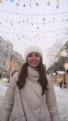 Beautiful woman with long brown hair, in warm winter clothes, standing on a snowy street in winter....