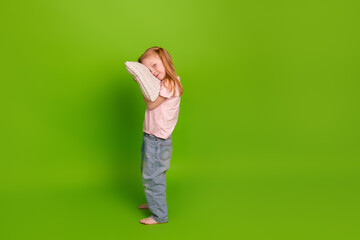 Charming girl with red hair holding a soft pillow against a vibrant green background spreading joy