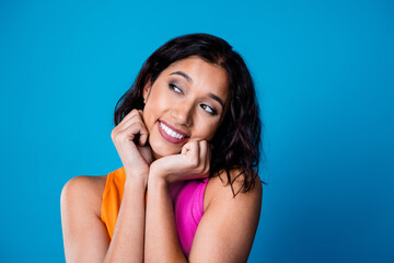 Charming young woman posing against bright blue background wearing colorful top and showing a...