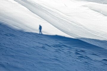 Shadow of a lone hiker cast on a snowy mountain slope. Minimalist winter landscape symbolizing...