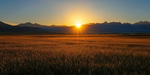 Fototapeta premium Sun dipping behind wheat-covered plains and towering twilight mountains