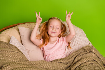 Adorable red-haired girl with pigtails posing on a cozy chair against a green background displaying...
