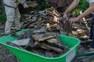Men and women work together to move wooden planks into a wheelbarrow outdoors.