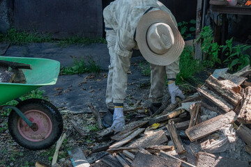 A person in protective clothing is picking up pieces of wood near a wheelbarrow.