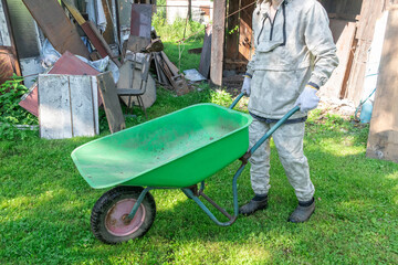 A person using a green wheelbarrow in a backyard, possibly for yard work or gardening.