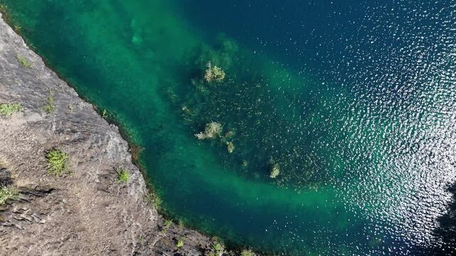 Drohnenflug &uuml;ber ein stillgelegten Steinbruch, dabei fliegt die Drohne im Spindelflug von unten nach oben. Die Aufnahme zeigt Wasser mit einer Gr&uuml;nfl&auml;che die aus dem Wasser w&auml;chst. Es war warm am Tag.