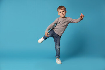 Happy little boy dancing on light blue background, space for text