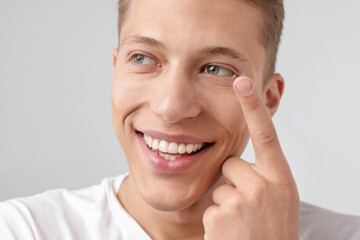Man putting in contact lens on light background, closeup