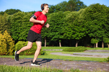 Sporty man with headphones running in park, space for text