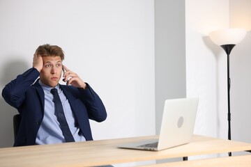 Young businessman with laptop complaining to someone via phone at wooden table indoors