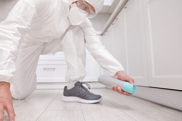 Pest control worker in protective suit spraying insecticide at home, closeup