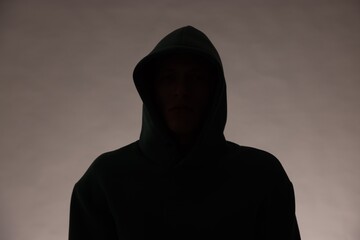 Silhouette of anonymous man in hood on grey background